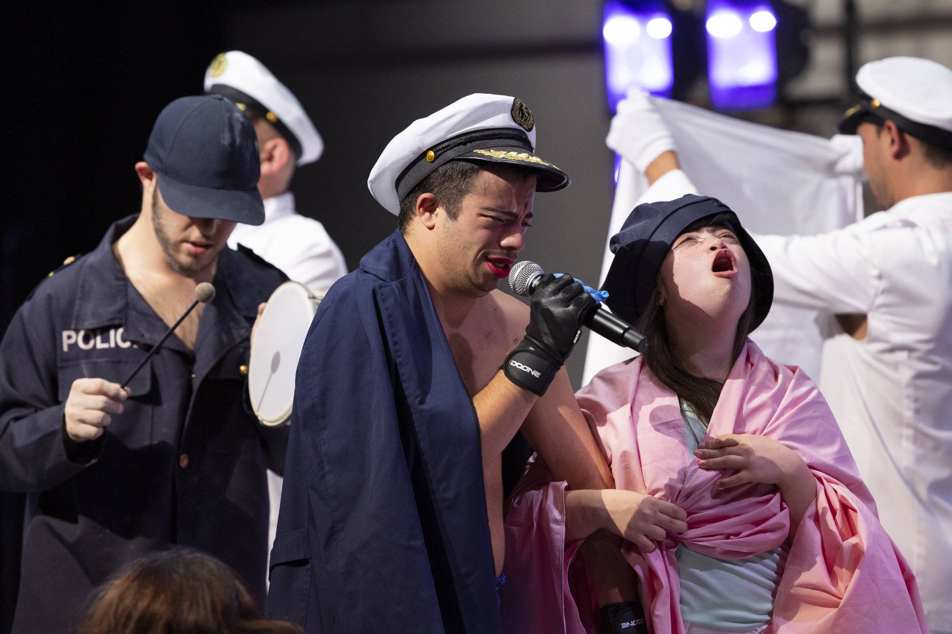 Vier Menschen in Uniform, einer Mischung aus Matrosen und Polizei, ziehen wie in einer Parade durch